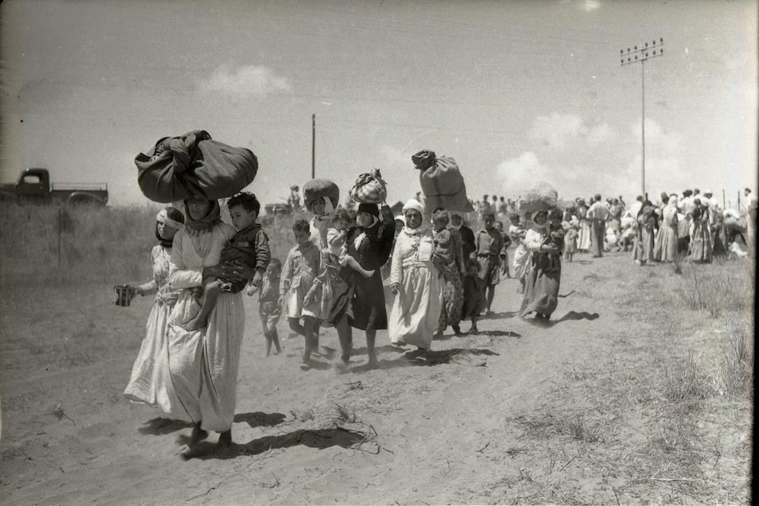 Femmes et enfants réfugiés victimes de la Nakba se suivant sur un chemin de terre, ils portent des chargements, des paquets. Cela fait suite au retrait des troupes britanniques suite à leur mandat.